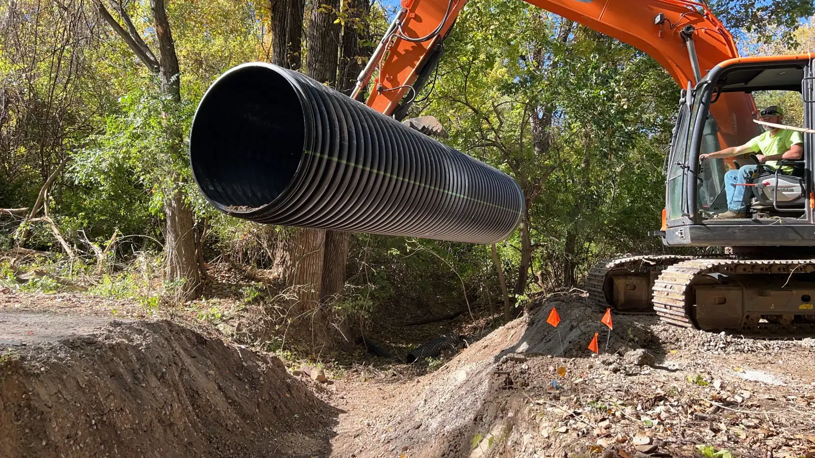 Crew installing a large corrugated culvert pipe to fix a drainage issue